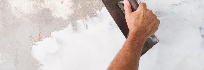 Person spachtelt Wand mit Spachtel