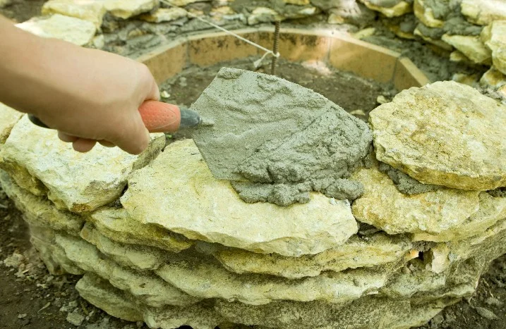 Person mauert Steine mit Kelle und Mörtel