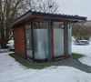 Eine moderne Außensauna mit Glasfront im verschneiten Garten.