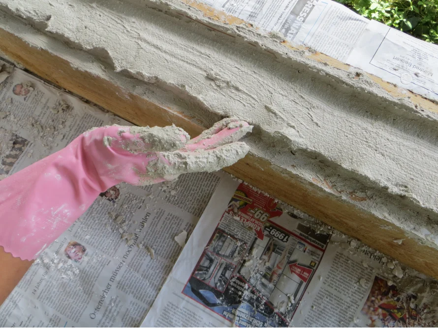Eine Hand mit einem rosa Handschuh trägt grauen Mörtel auf