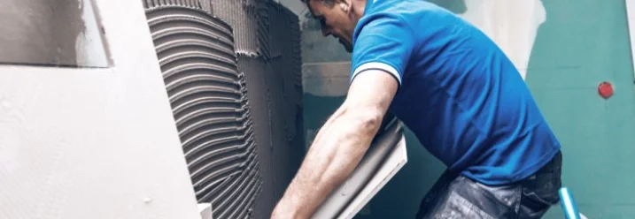 Person verlegt Fliese an Wand.