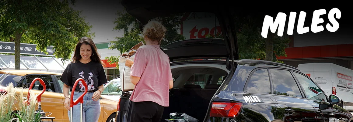 Zwei Personen laden Einkäufe in einen schwarzen Kombi