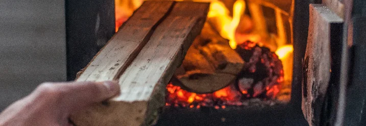 Hand legt Holzscheit in Kaminofen