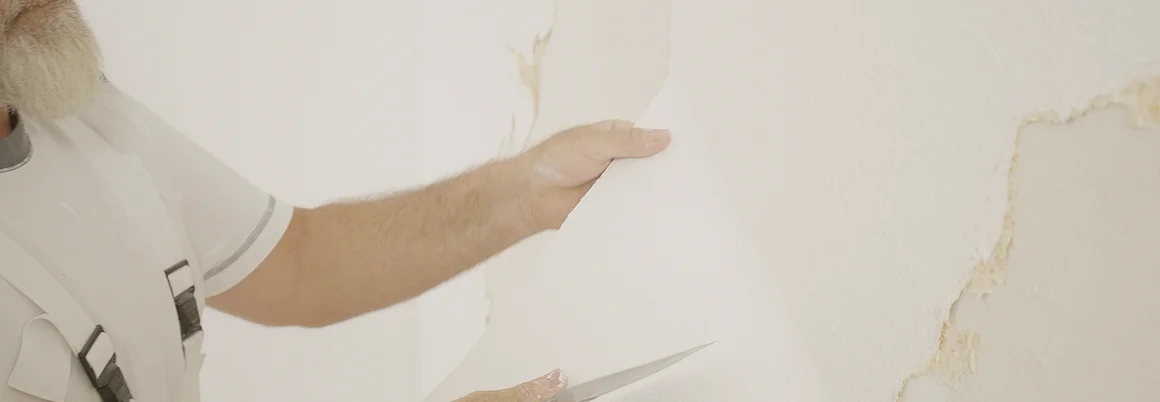 Person entfernt Tapete mit Spachtel.