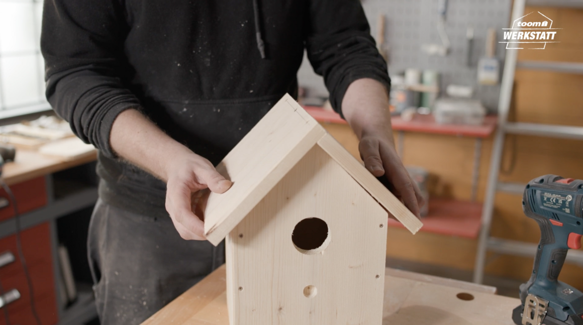Person baut einen Nistkasten aus Holz zusammen