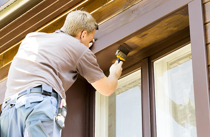 Person streicht Fensterrahmen mit Pinsel.