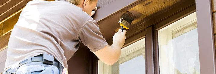 Person streicht Fensterrahmen mit Pinsel.