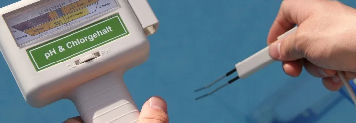 Eine Person hält ein elektronisches Messgerät an einen Swimmingpool.