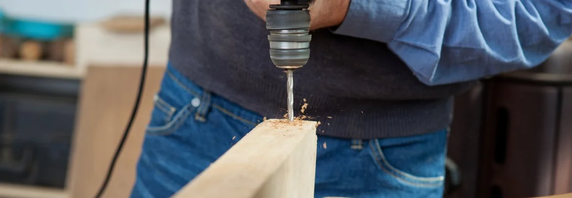 Eine Person bohrt mit einer Bohrmaschine in ein Holzbrett.