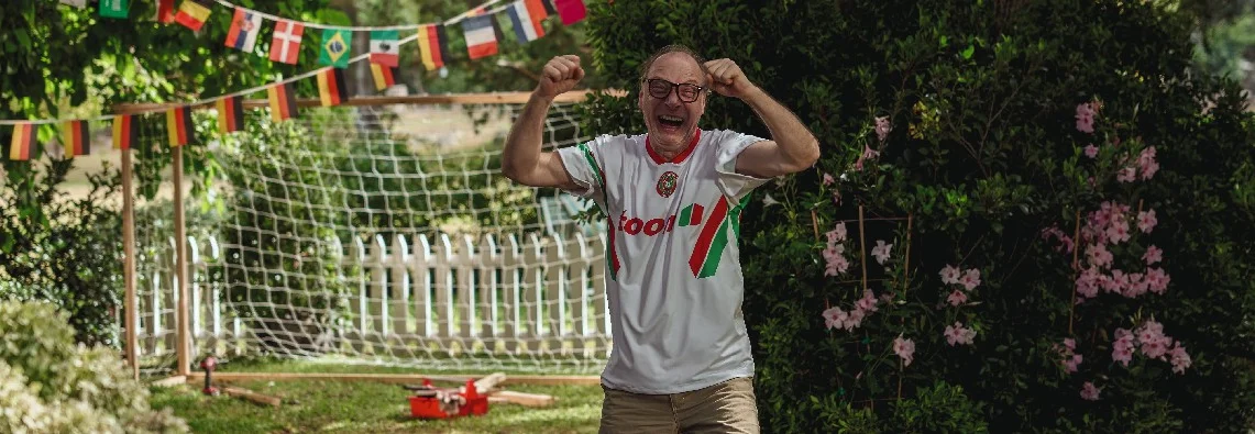 Jubelnder Mensch im Trikot vor einem Fußballtor im Garten.