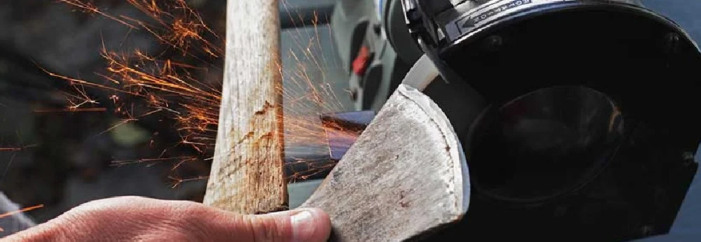 Person schleift Axt mit Schleifmaschine