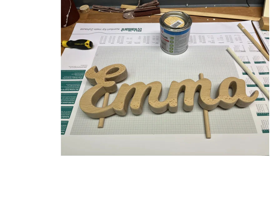 Der Schriftzug "Emma" aus Holz liegt auf einer Werkbank.