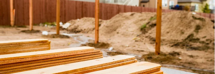 Holzlatten im Vordergrund, im Hintergrund ein Gartenzaun und Häuser.