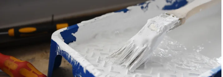 Pinsel in blauer Farbwanne mit weißer Farbe