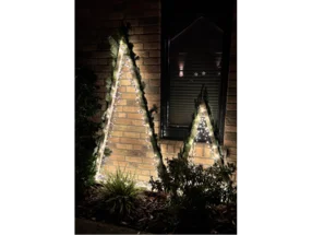 Zwei beleuchtete, hölzerne Weihnachtsbäume vor einem Haus.