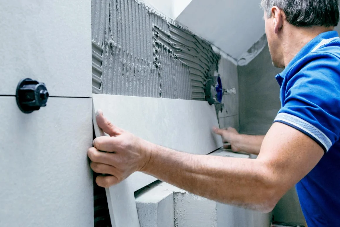 Person bringt Fliese an Wand an