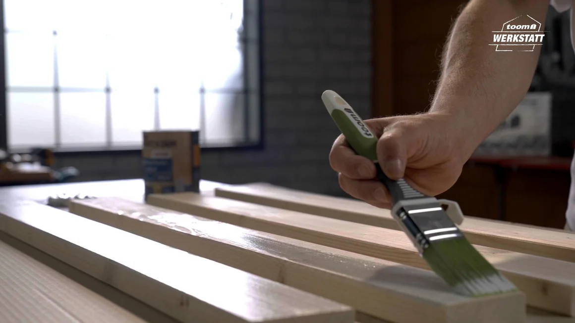 Person streicht Holzbalken mit Pinsel