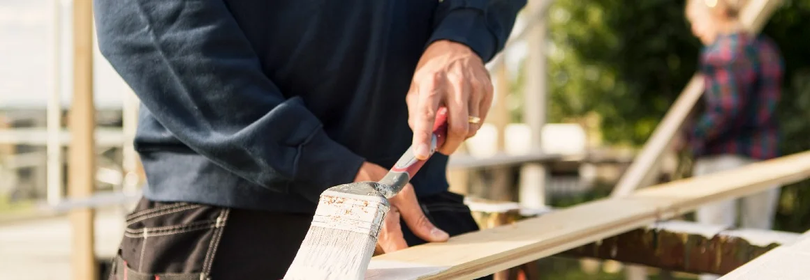 Person streicht Holzbrett mit Pinsel