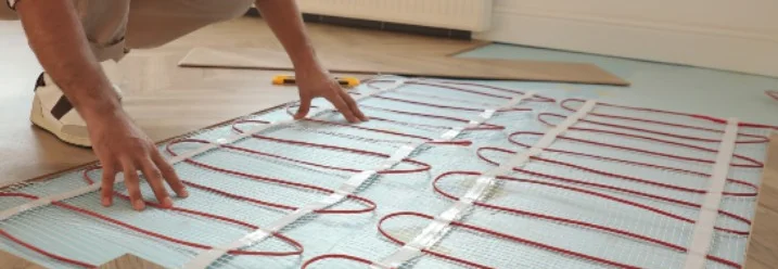 Person verlegt Fußbodenheizung auf Fliesen.