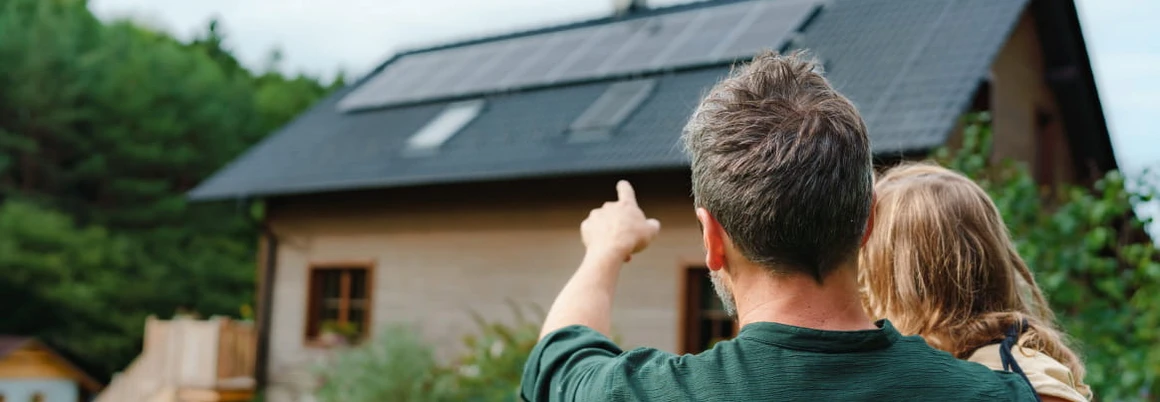 Eine Person zeigt auf eine Solaranlage auf einem Hausdach.