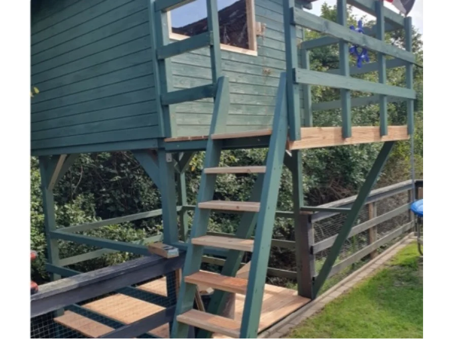 Grünes Spielhaus aus Holz mit Leiter und Balkon.