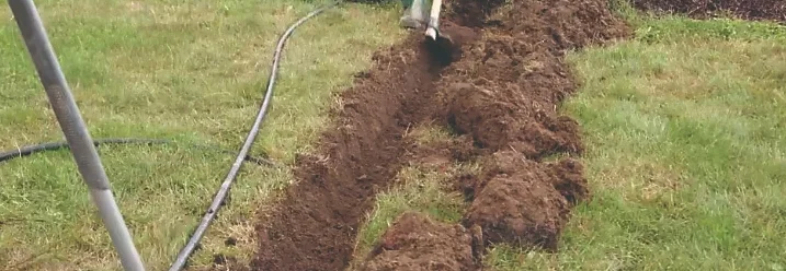 Person gräbt mit Spaten einen Graben in Rasenfläche