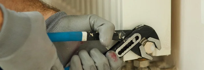 Person montiert Heizkörper mit Rohrzange.