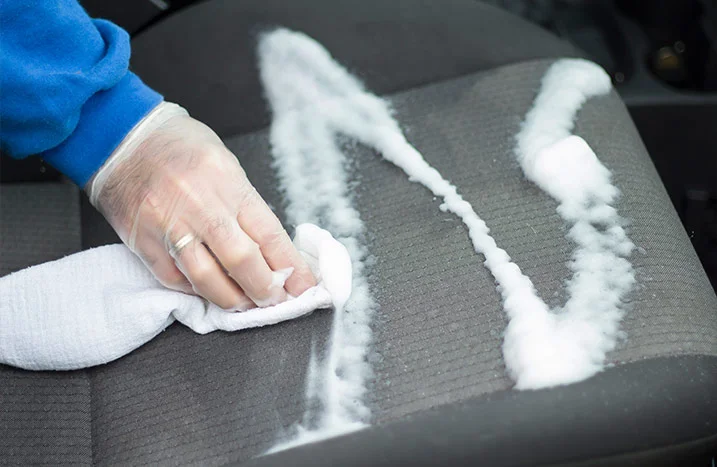 Person reinigt Autositz mit Tuch