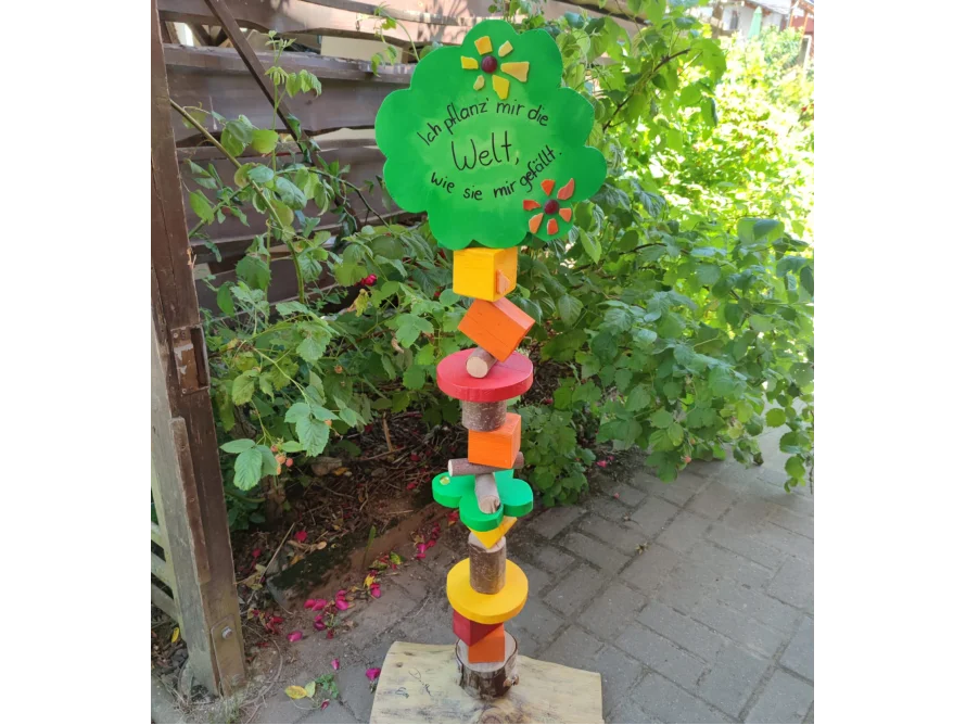 Bunte, selbstgemachte Holzskulptur mit Aufschrift steht im Garten.