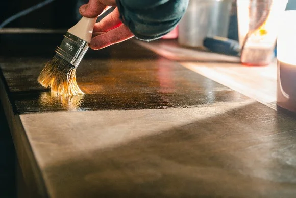 Person streicht Holzplatte mit Pinsel