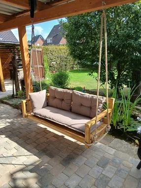Hölzerne Hollywoodschaukel mit grauen Polstern auf einer Terrasse.