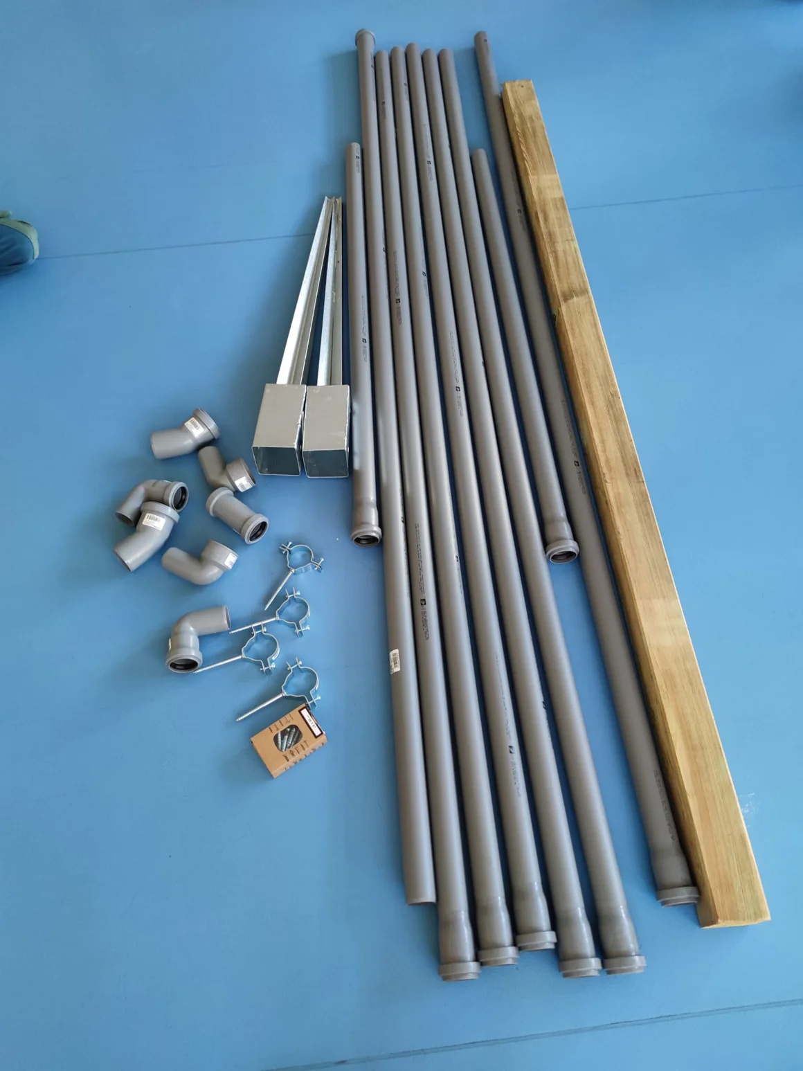 Auf einem blauen Boden liegen Rohre, ein Holzbalken und Montagematerial.