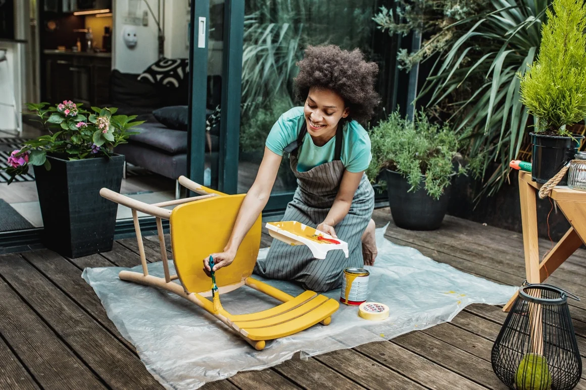 Person streicht Stuhl gelb.