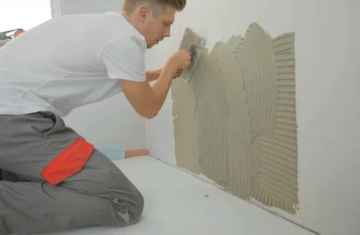 Person trägt Kleber mit Kelle an Wand auf