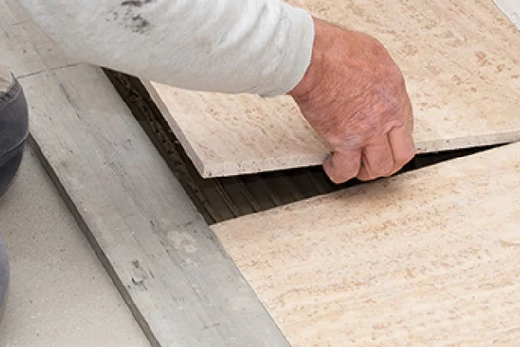 Person verlegt Fliesen mit Hammer