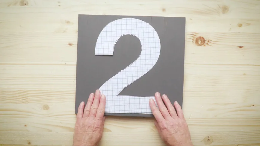 Zwei Hände halten Papierschablone auf Holz