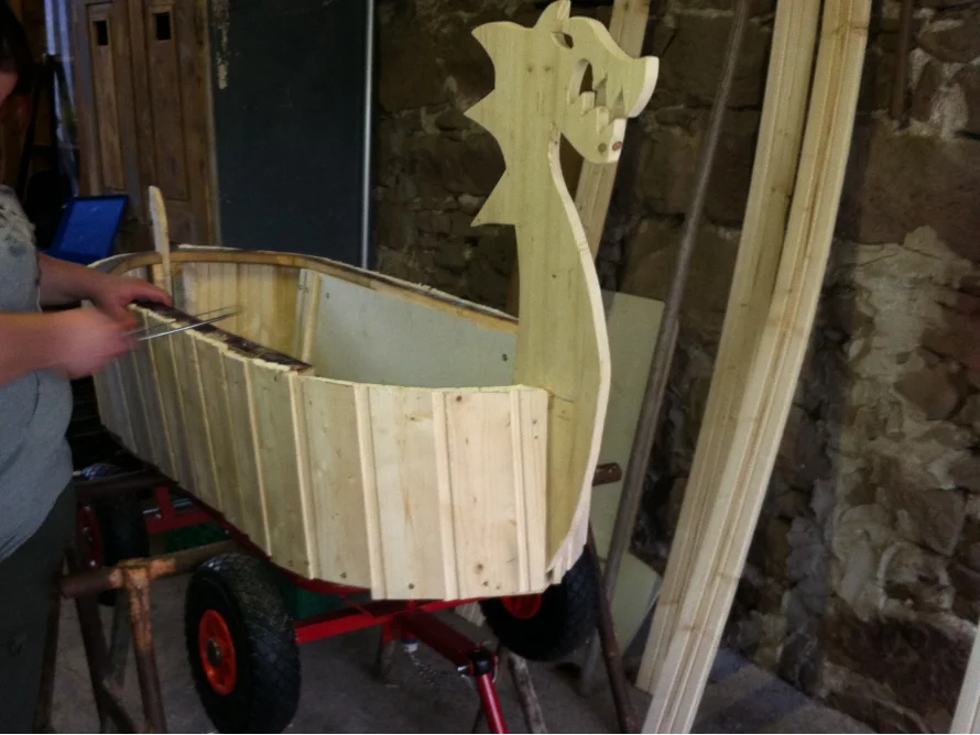 Person baut einen Holz-Wagen in Form eines Wikingerschiffs