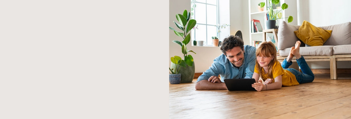 Kind und Mann liegt auf Holzboden mit Sofa im Hintergrund.