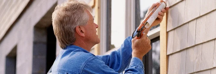 Person dichtet Fenster mit Dichtungsmittel ab