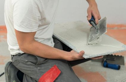 Natursteine richtig verlegen Handwerker trägt Fliesenkleber auf die Rückseite einer Natursteinfliese auf.