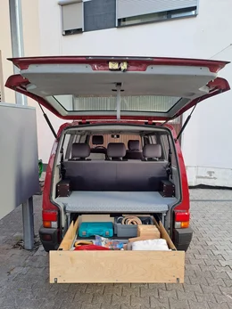 Campingausbau in einem roten Bus mit großer Schublade.
