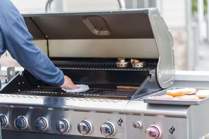 Person reinigt Grill mit Tuch