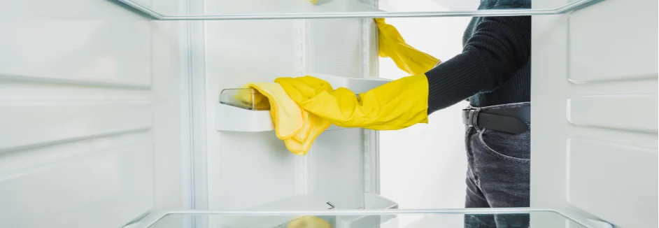 Person reinigt Kühlschrank mit Tuch.