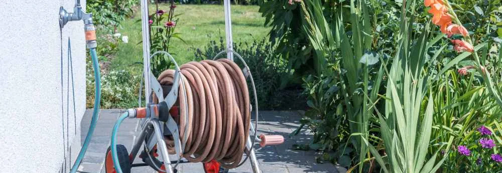Ein aufgerollter Gartenschlauch auf einem Schlauchwagen steht im Garten an einer Hauswand.