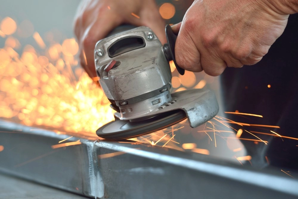 Eine Person schleift mit einem Winkelschleifer Metall, es sprühen Funken.