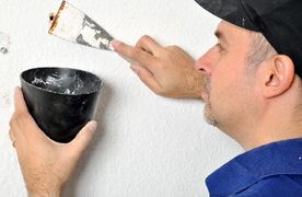 Ein Mann verspachtelt ein Bohrloch in einer weißen Wand.