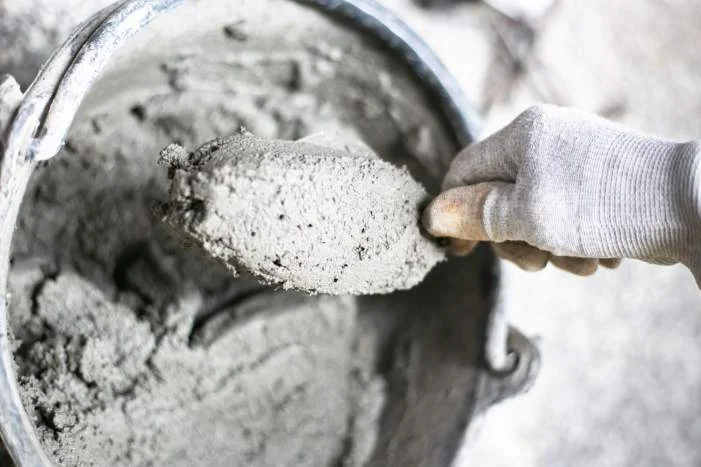 Hand mit Kelle hebt Zement aus Eimer