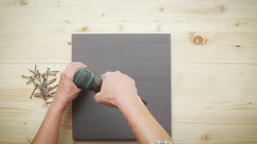 Person schraubt Holzplatte auf.