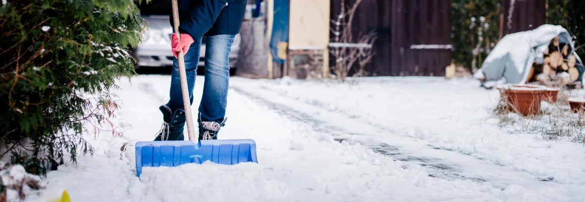 Person räumt Schnee mit Schneeschieber
