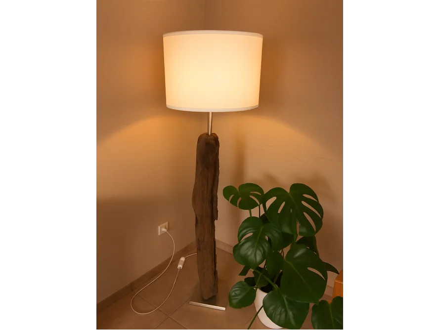 Eine beleuchtete Stehlampe mit einem Fuß aus Holz neben einer Zimmerpflanze.